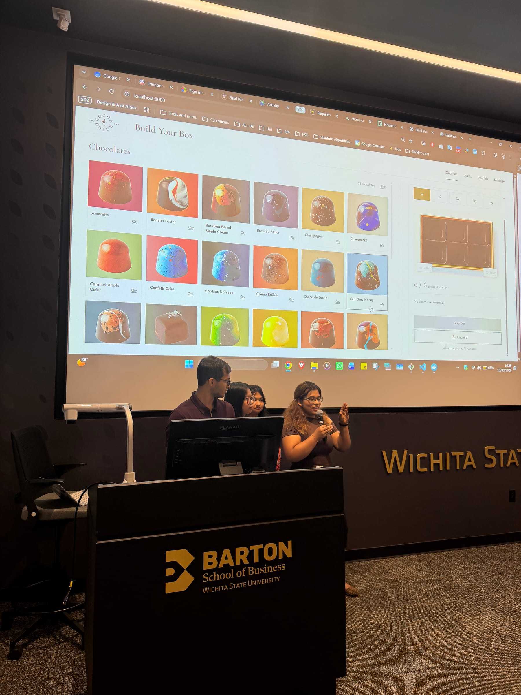 Three students at the Barton School of Business podium demo a Build Your Box chocolate-ordering app on the big screen.