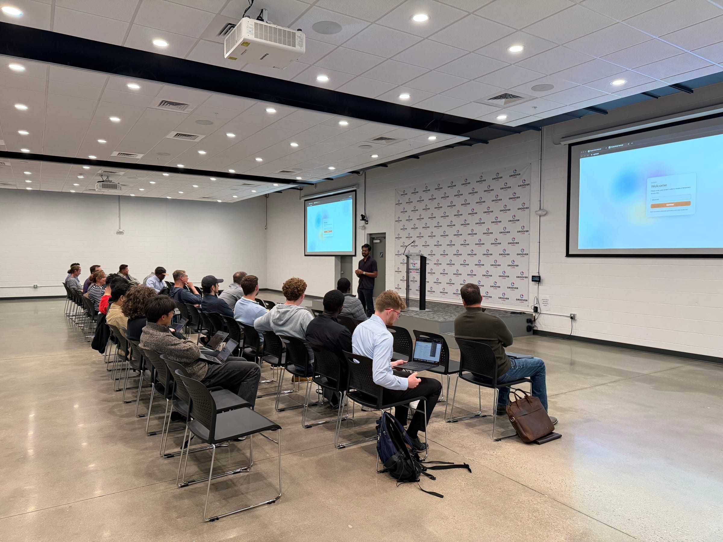 A speaker at a podium presents to rows of attendees at Groover Labs.